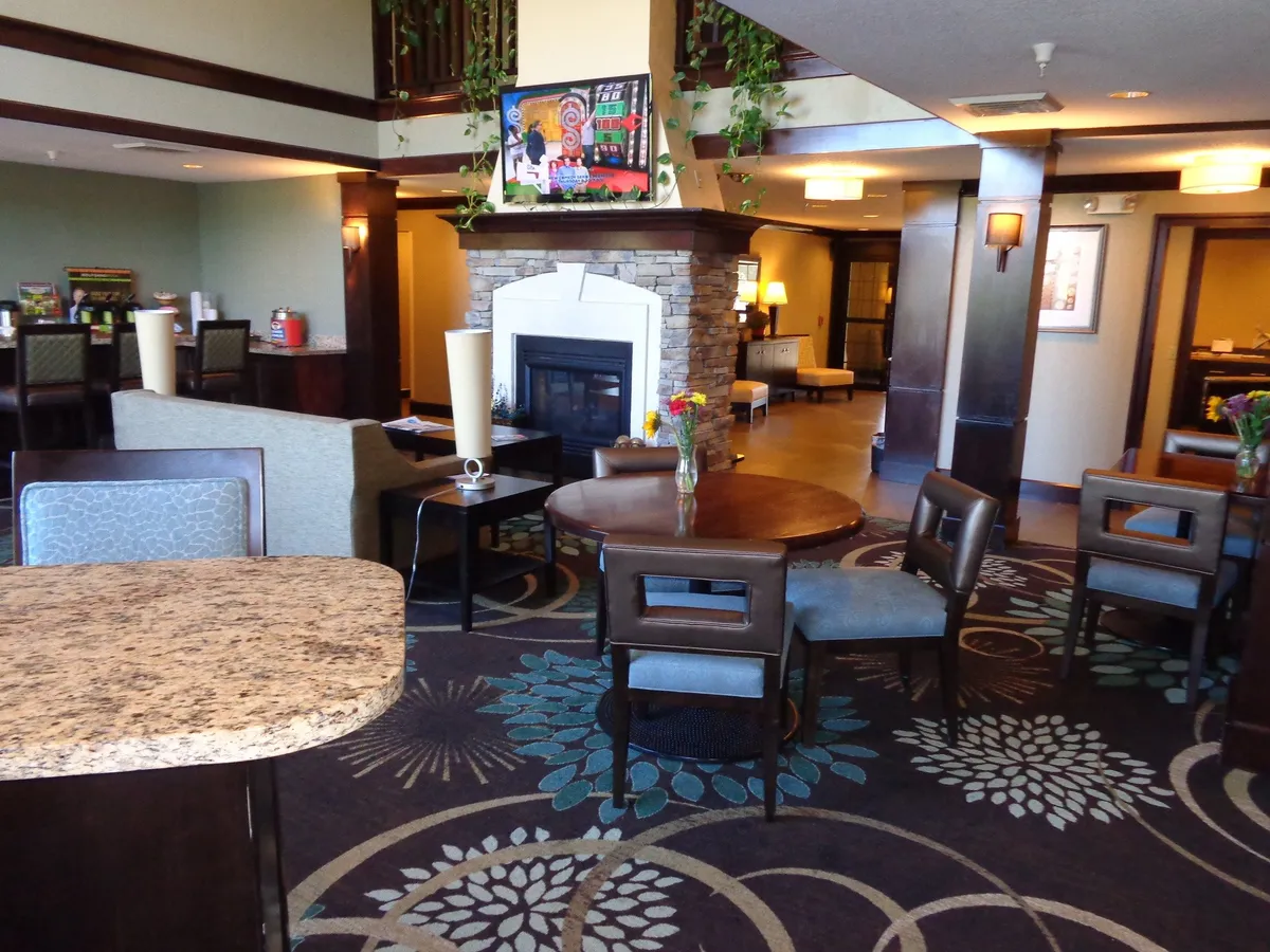 A warm and inviting communal area showcasing a fireplace, tasteful artwork, and several dining tables. The setting suggests a comfortable spot for relaxing solo or socializing with family or friends, with the cozy fireplace offering an additional touch of home-like comfort.